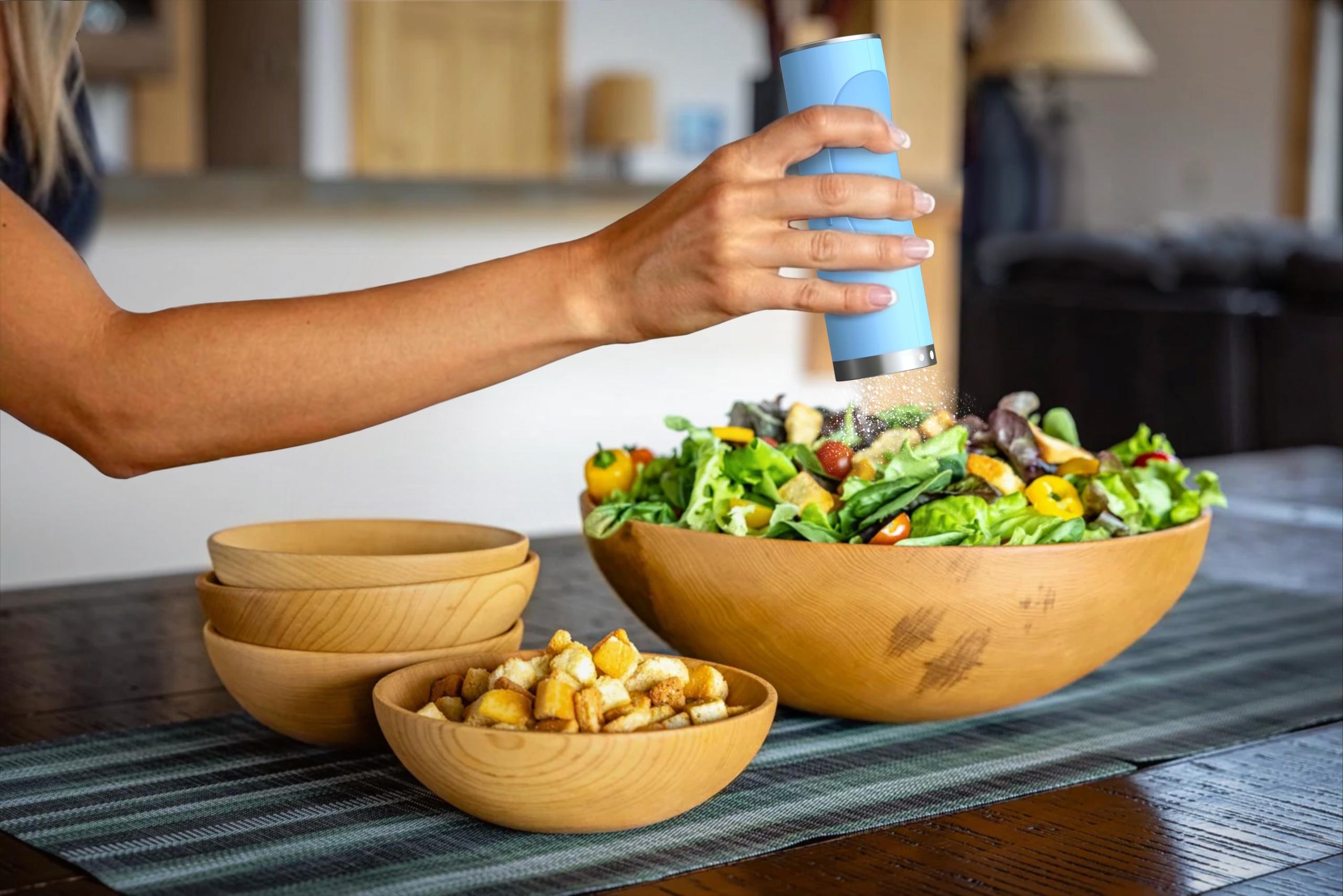 Hand sprinkling spice from the Smeg-branded handheld grinder over a salad